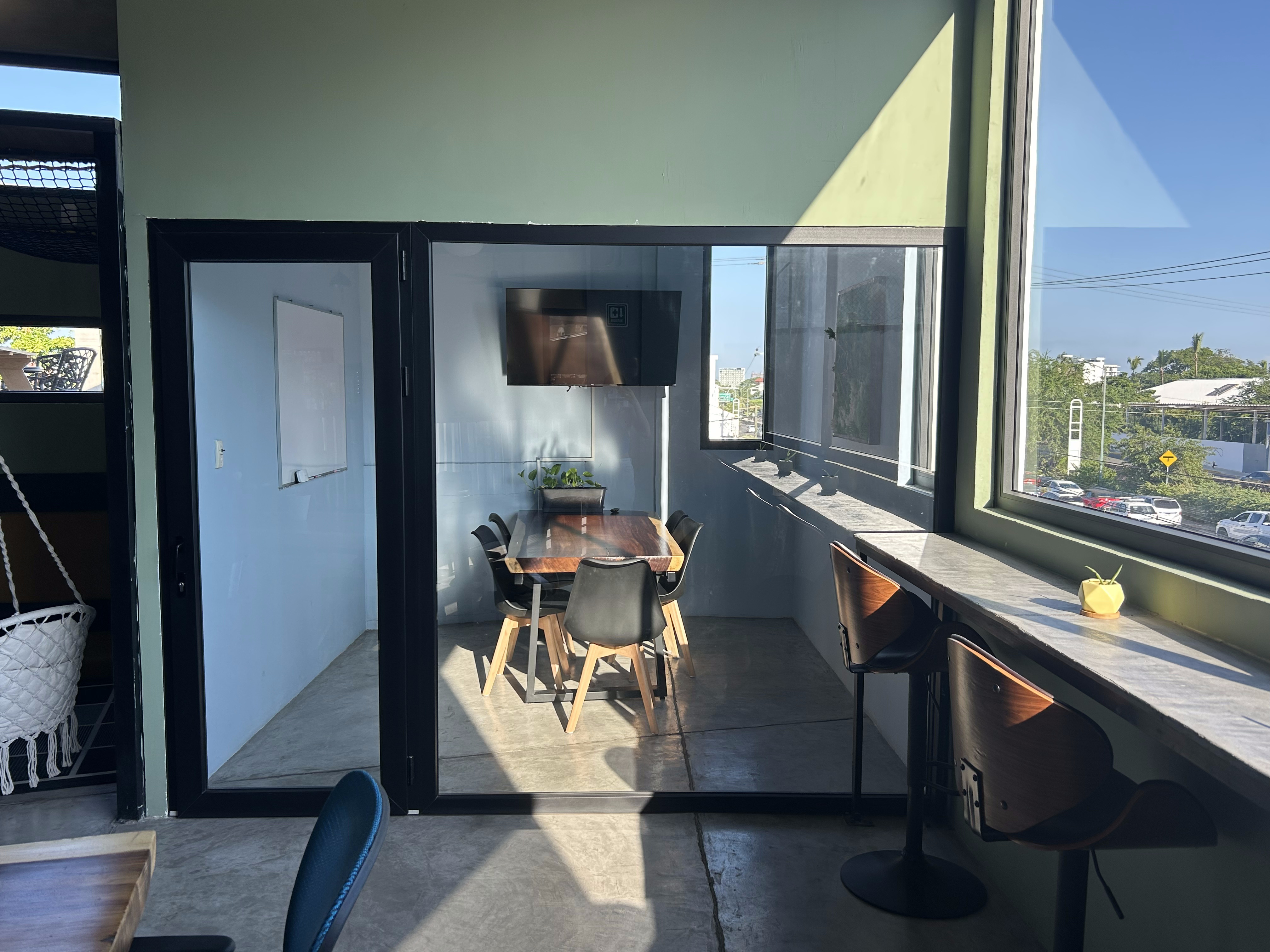 A well-lit meeting room with a long table, multiple chairs, and a large window providing natural light.